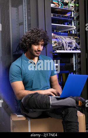 Computer programmer using laptop sitting on box in server room Stock Photo