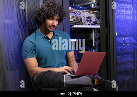 Technician using laptop sitting in server room Stock Photo