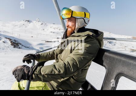 Young man wearing ski helmet and goggles sitting on lift Stock Photo
