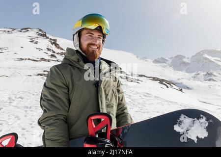 Happy young man wearing ski goggles holding snowboard on sunny day Stock Photo