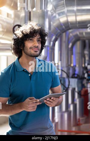 Happy technician holding tablet PC standing in factory Stock Photo