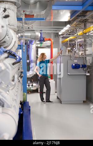 Technician standing with hand in pocket checking machine in factory Stock Photo