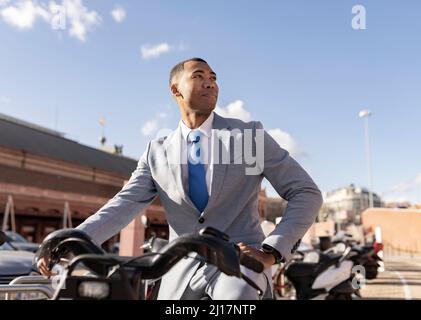Businessman sitting on electric bicycle on sunny day Stock Photo