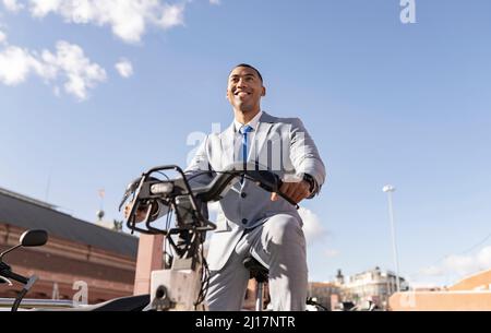 Happy businessman sitting on electric bicycle on sunny day Stock Photo
