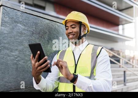 Smiling engineer using tablet PC standing by wall Stock Photo