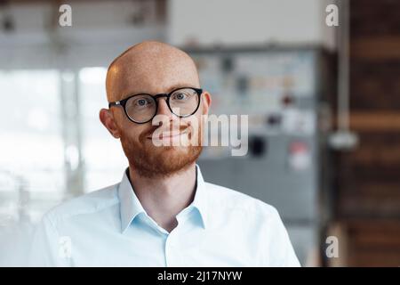 Smiling young bald working man wearing eyeglasses in office Stock Photo