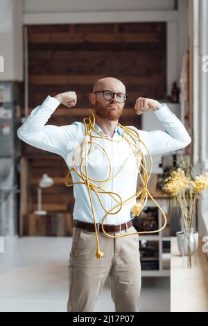 Confident young businessman covered with cable flexing muscles in office Stock Photo