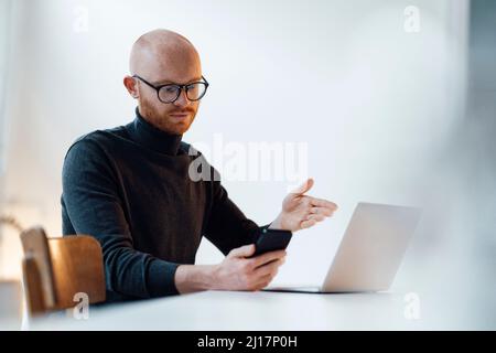 Young businessman using smartphone sitting with laptop working in office Stock Photo