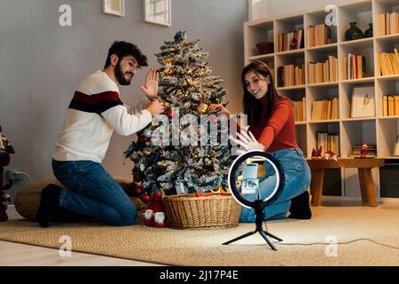 Happy young couple waving hands vlogging through mobile phone at home Stock Photo