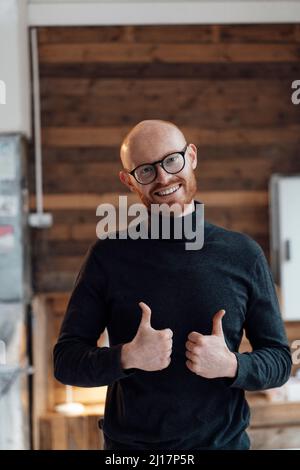 Happy young working man gesturing thumbs up in office Stock Photo