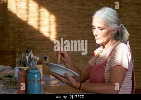 Woman painting clay plate sitting at table Stock Photo