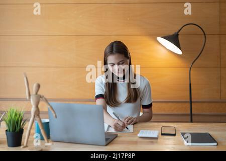 Young asian accountant taking note on notepad and using a laptop computer, calculator for financial. Stock Photo
