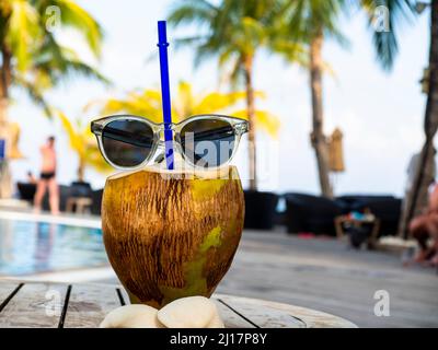 Sunglasses on top of cracked coconut with drinking straw inside Stock Photo