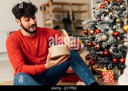 Surprised young man opening Christmas present at home Stock Photo