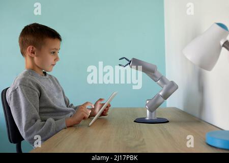 Boy controlling robotic arm through tablet PC sitting at table Stock Photo