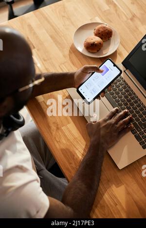 Man with laptop using app on smart phone at home Stock Photo