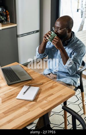 Businessman drinking tea looking at laptop on dining table at home Stock Photo