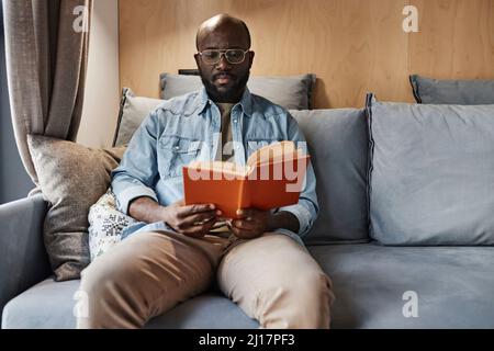 Man reading novel sitting on sofa at home Stock Photo