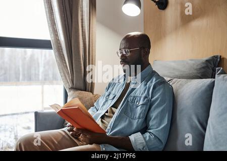 Young man reading novel on sofa at home Stock Photo