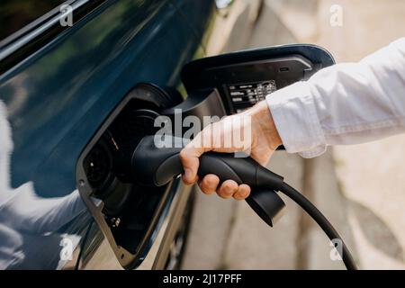 Man holding electric plug of hybrid car at charging point Stock Photo