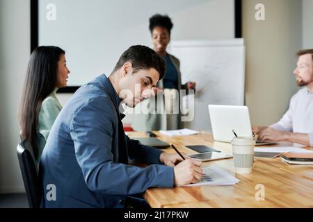 Young businessman making notes sitting at desk in meeting at office Stock Photo