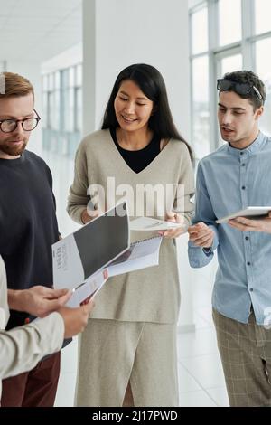 Multi-ethnic group of business colleagues discussing over reports standing in office Stock Photo