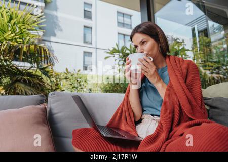 Freelancer with laptop drinking coffee at yard Stock Photo