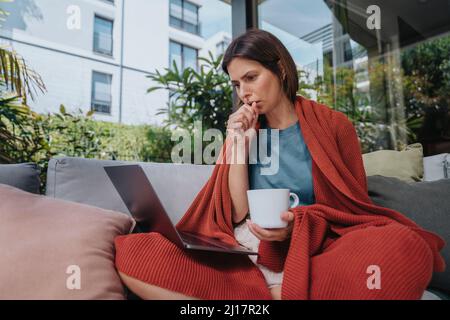 Sick businesswoman coughing and working on laptop in yard Stock Photo