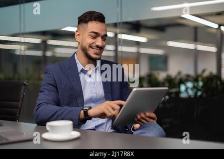 Happy middle eastern businessman working at office, using digital tablet Stock Photo
