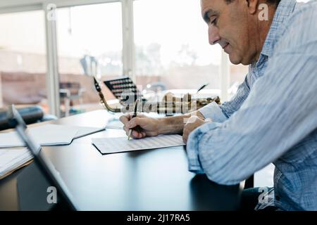 Man writing musical notes on paper sitting at table Stock Photo