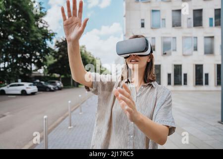 Woman gesturing wearing virtual reality headset in front of building Stock Photo