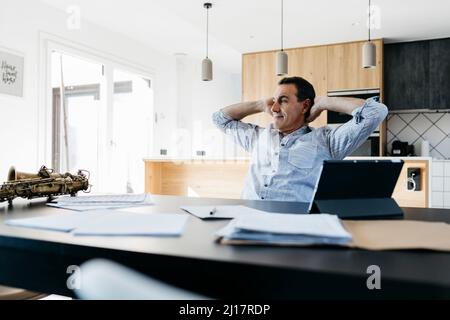 Smiling man sitting with hands behind head in kitchen at table Stock Photo