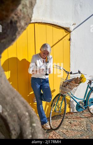 Happy woman with camera standing in front of yellow door Stock Photo