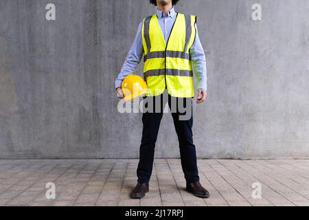 Man wearing reflective clothing holding hardhat standing in front of wall Stock Photo