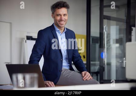 Happy businessman sitting on desk at work place Stock Photo