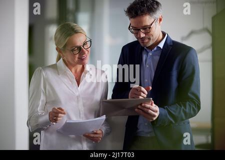 Smiling businesswoman holding document discussing with colleague using tablet PC in office Stock Photo