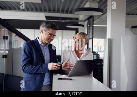 Business colleagues sharing ideas working on laptop in office Stock Photo