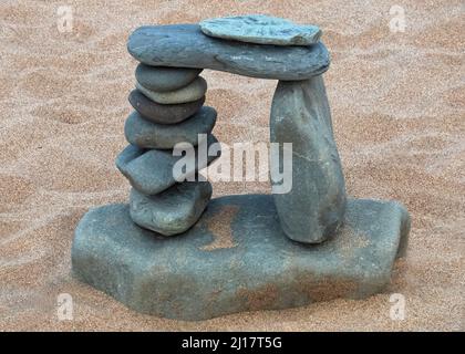 Colour photograph of coastal stones on beach stacked in almost a Stonehenge design. Stones smoothed and rounded by the passages of time and tide conta Stock Photo