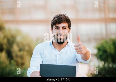 Smiling freelancer with laptop gesturing thumbs up Stock Photo