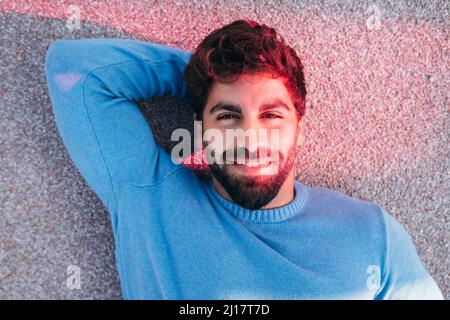 Smiling young man with hand behind head lying on back Stock Photo
