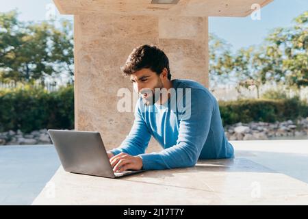 Smiling young man using laptop leaning on wall Stock Photo