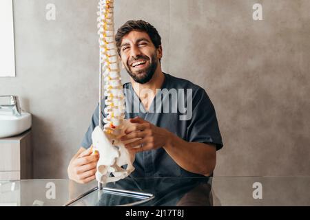 Happy young physiotherapist with human spine model at medical clinic Stock Photo