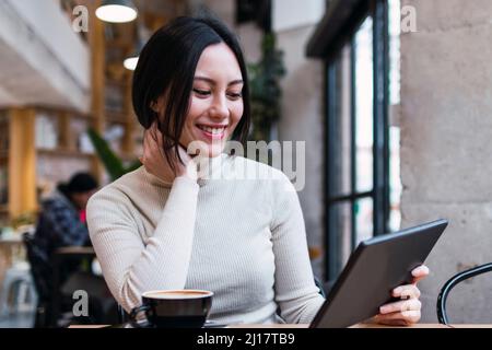 Smiling woman holding tablet PC sitting at cafe Stock Photo