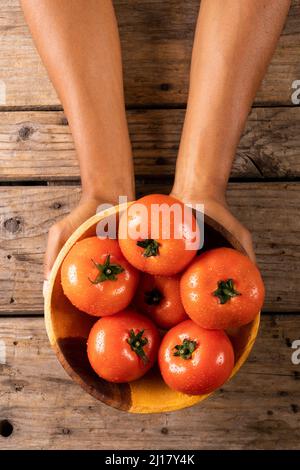 Overhead view of man's hands holding bowl full of fresh tomatoes in bowl on wooden table Stock Photo