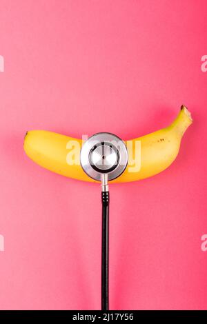 Overhead view of fresh banana with stethoscope by copy space on pink background Stock Photo