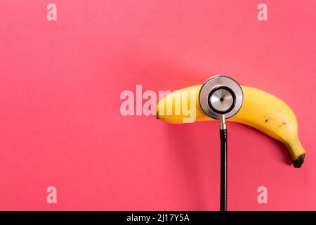 Overhead view of fresh banana with stethoscope by copy space over pink background Stock Photo