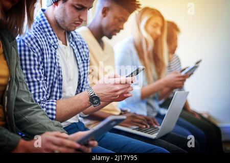 Catching up with their connections between classes. Shot of a group of university students using their digital devices at campus. Stock Photo