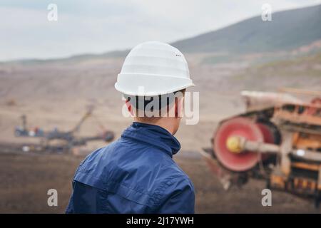 Coal mining in surface mine. Miner looking on the huge excavator. Stock Photo