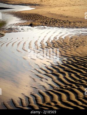 Colour photograph containing tidal sand patterns and reflections with varying textures and colours on the wetter sand at the National Trust owned Penb Stock Photo