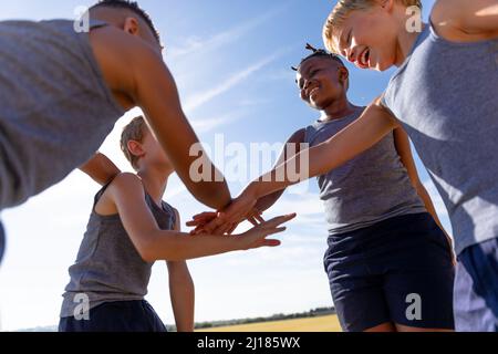 Smiling multiracial elementary schoolboys stacking hands during soccer match against sky Stock Photo